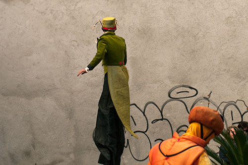 Hombre sobre zancos, de espalda, delante de su pared - © Norbert Pousseur